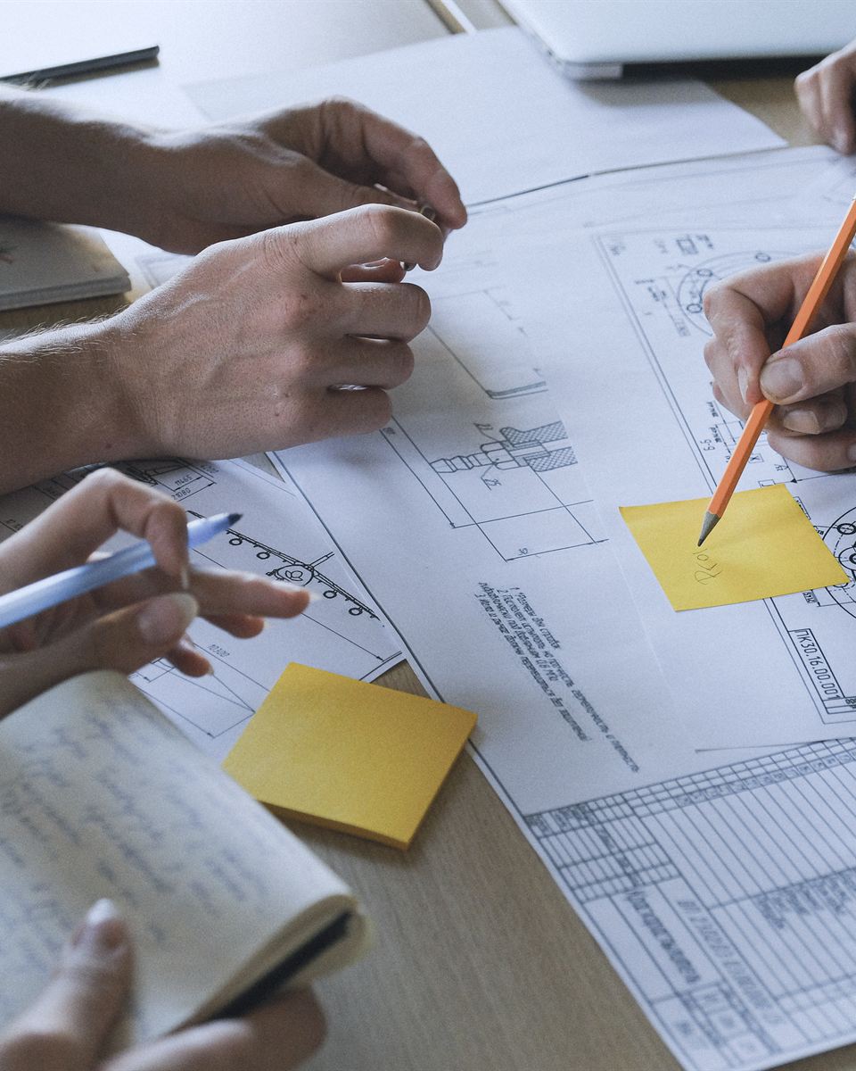 Mãos sobre desenhos técnicos e anotações durante o planejamento de um projeto