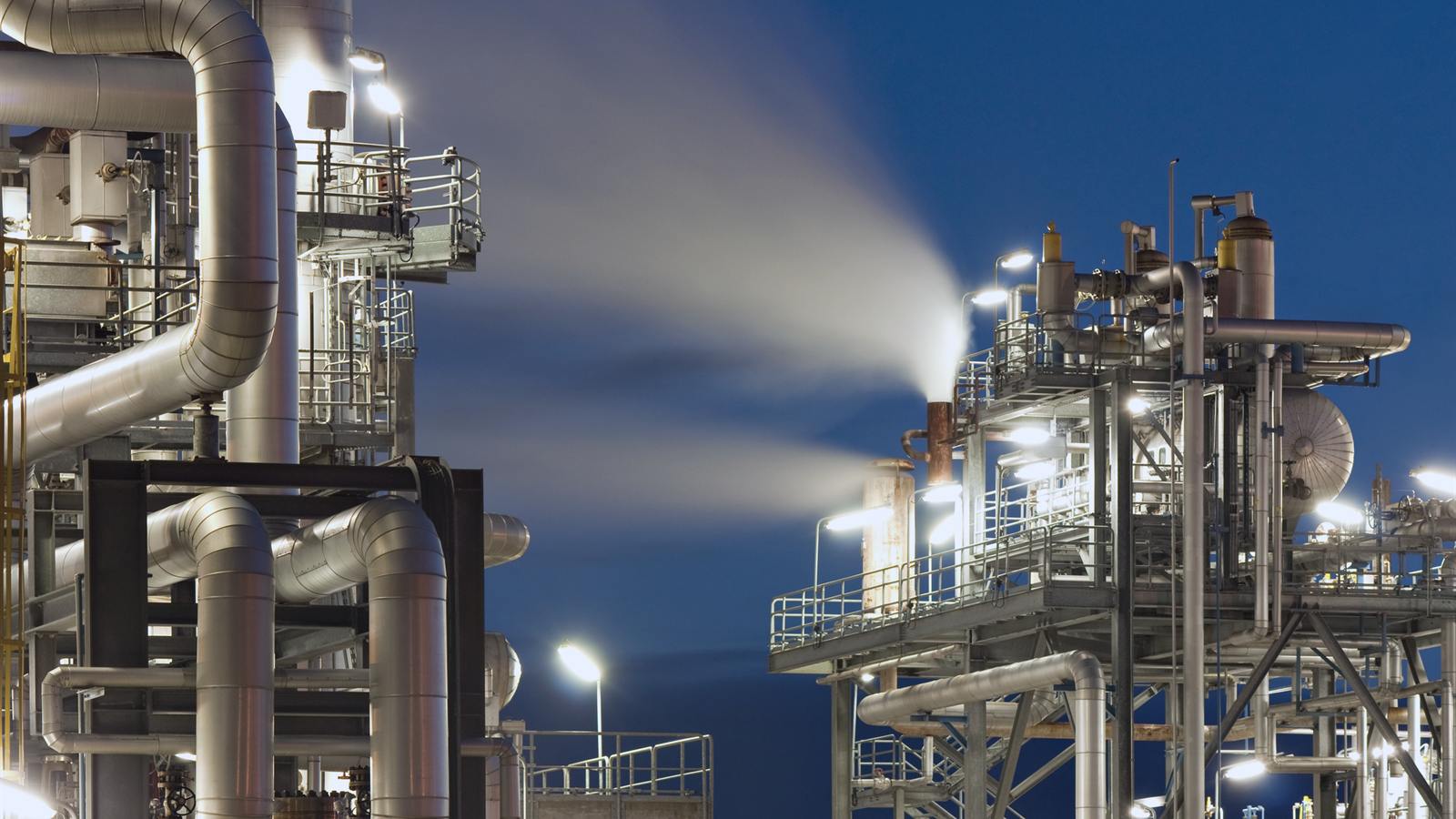 Planta de processo iluminada à noite, com tubulações e plataformas