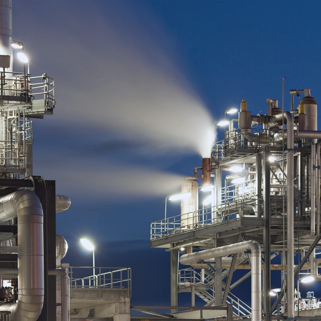 Planta industrial iluminada à noite, com tubulações e estruturas metálicas