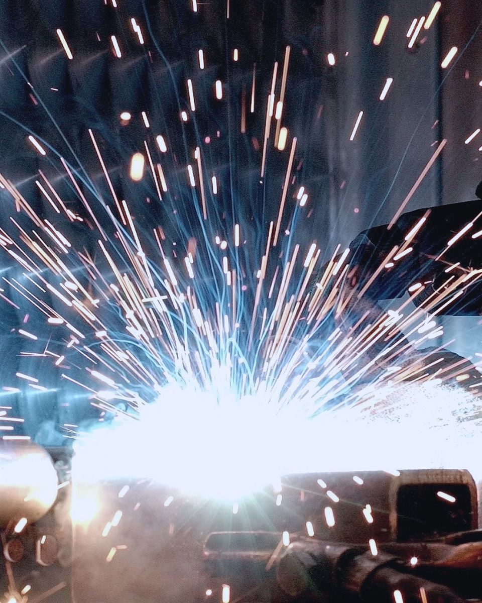 Faíscas de soldagem em oficina industrial, com luva de proteção em primeiro plano